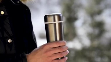 Closeup view of woman opening lid of thermo bottle in winter