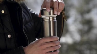 Closeup view of woman closing lid of thermo bottle in winter