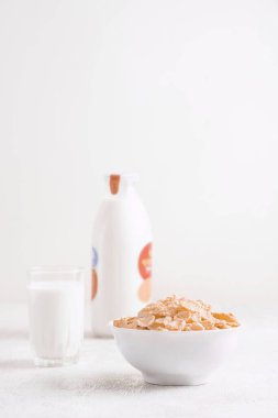 Bir kase mısır gevreği, sütlü, taze ahududu, yabanmersini. Sağlıklı kahvaltı için bir sürahi süt ve beyaz tahta üzerinde bir bardak.