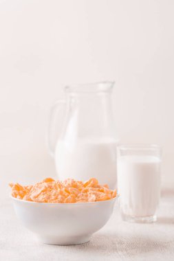 Bir kase mısır gevreği, sütlü, taze ahududu, yabanmersini. Sağlıklı kahvaltı için bir sürahi süt ve beyaz tahta üzerinde bir bardak.