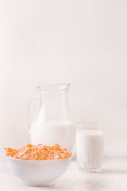 Bir kase mısır gevreği, sütlü, taze ahududu, yabanmersini. Sağlıklı kahvaltı için bir sürahi süt ve beyaz tahta üzerinde bir bardak.