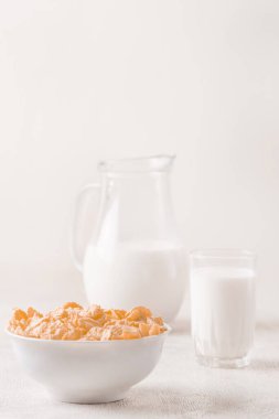 Bir kase mısır gevreği, sütlü, taze ahududu, yabanmersini. Sağlıklı kahvaltı için bir sürahi süt ve beyaz tahta üzerinde bir bardak.