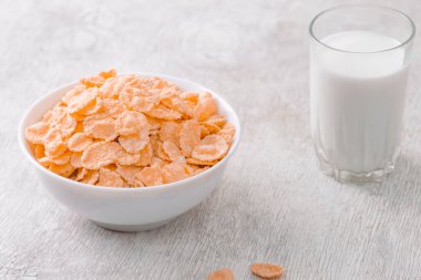 Bir kase mısır gevreği, sütlü, taze ahududu, yabanmersini. Sağlıklı kahvaltı için bir sürahi süt ve beyaz tahta üzerinde bir bardak.