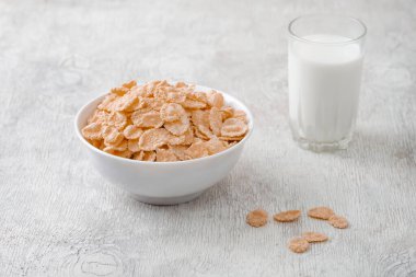 Bir kase mısır gevreği, sütlü, taze ahududu, yabanmersini. Sağlıklı kahvaltı için bir sürahi süt ve beyaz tahta üzerinde bir bardak.