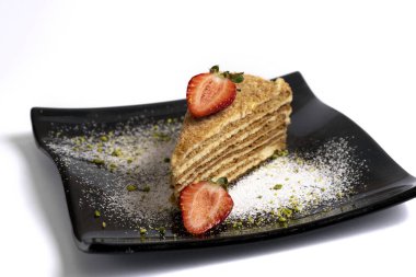 Beyaz arka planda izole edilmiş siyah bir tabakta çilekli katman sünger kek.