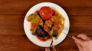 Bir adam et ile doldurulmuş yaz dolması, lahana, patlıcan, biber ve domates yer