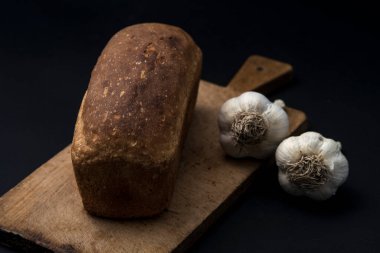 Karanlık ekmek ve siyah bir zemin üzerine sarımsak.