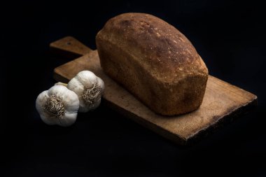 Karanlık ekmek ve siyah bir zemin üzerine sarımsak.