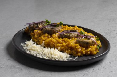 Pumpkin risotto with mushrooms and parmesan cheese on black plate