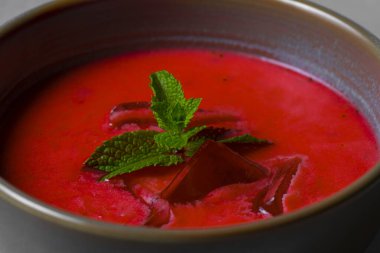 Cold beetroot soup with mint in a bowl on a gray background