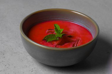Cold beetroot soup with mint in a bowl on a gray background