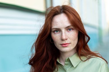 Uzun kızıl saçlı genç bir kadın şehirde poz veriyor. Çilli yüz, yakından, doğal güzellik. Açık havada fotoekonomik durgunluk