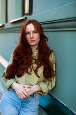 Uzun kızıl saçlı genç bir kadın şehirde poz veriyor. Çilli yüz, yakından, doğal güzellik. Açık havada fotoekonomik durgunluk