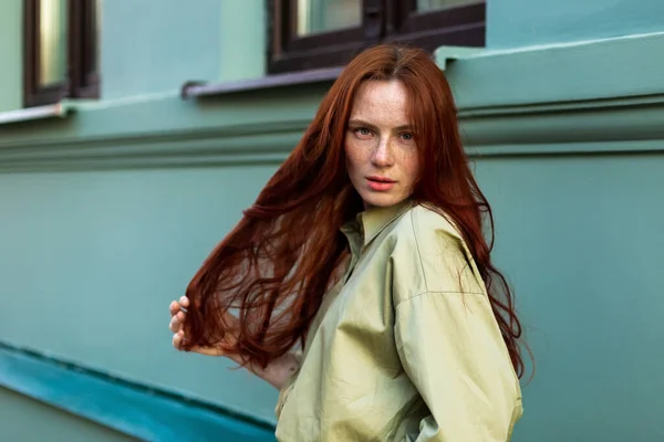 Young woman with long ginger hair posing  in city. Freckled face close up, natural beauty face. Outdoor photosession