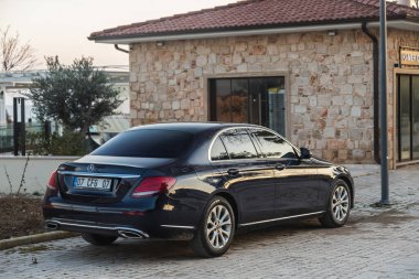 Side, Turkey -January 21, 2023:     black Mercedes-Benz E-class  e180 is parked  on the street on a warm  day against the backdrop of a shops, hotel
