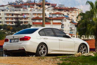 Alanya, Turkey  April 17 2021:  white  BMW 3-series 320i  is parked  on the street in city against the backdrop of a buildung,  shops 