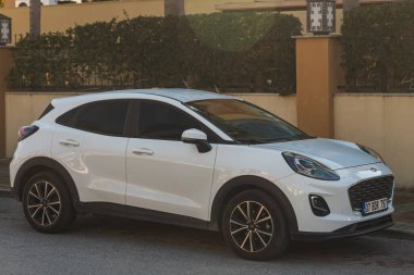 Yana, Türkiye - 23 Ocak 2023: Ilık bir yaz gününde beyaz Ford Puma, bir binanın, çitin zeminine park etti.