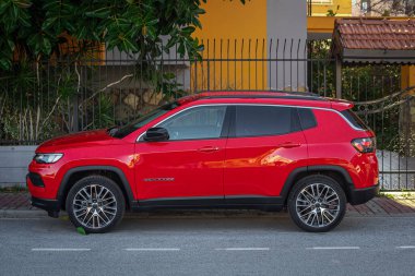 Yana, Türkiye - 05 Şubat 2023: Kırmızı cip pusulası sıcak bir yaz gününde bir caddenin arka planına park edilmiştir. 