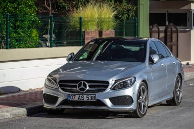 ; Türkiye 05 Şubat 2023: Gümüş Mercedes-Benz C sınıfı sıcak bir günde bir binanın arka planına, ağaçlara karşı sokağa park edildi 