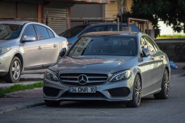 ; Türkiye 05 Şubat 2023: Gümüş Mercedes-Benz C sınıfı sıcak bir günde bir binanın arka planına, ağaçlara karşı sokağa park edildi 