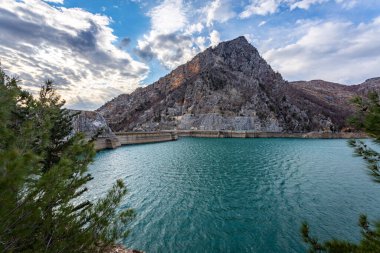 Bir dağ gölünün panoramik manzarası. Temiz turkuaz yeşili su, arka planda bir yol ve çiftçi köyü.