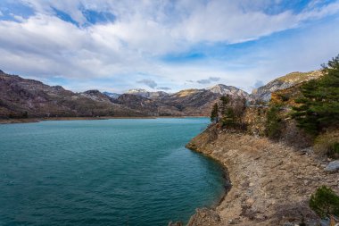 Bir dağ gölünün panoramik manzarası. Temiz turkuaz yeşili su, arka planda bir yol ve çiftçi köyü.