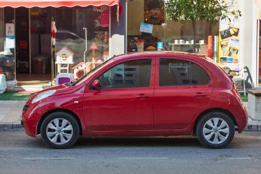 Yan, Türkiye 11 Şubat 2023: Kırmızı Nissan March sıcak bir günde bir parkın arka planına park etti 