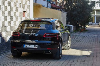 Yan, Türkiye 11 Şubat 2023: Siyah Porsche Macan, sıcak bir günde bir inşaat tezgahına, dükkanlara karşı sokağa park etti 