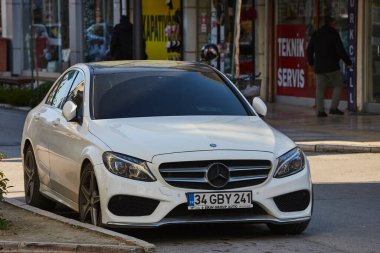 ; Türkiye 11 Şubat 2023: Beyaz Mercedes-Benz C sınıfı sıcak bir günde bir binanın zeminine, ağaçlara karşı sokağa park edilmiştir. 