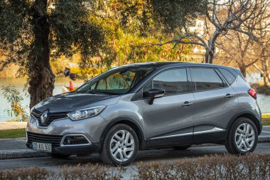Yan, Türkiye 13 Şubat 2023: Gümüş Renault Kaptur, sıcak bir günde bir ağaçların arka planına karşı sokağa park etti.  