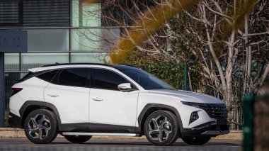 Taraf; Türkiye 18 Şubat 2023: Beyaz Hyundai Tucson, sıcak bir günde otosalonun arka planına karşı sokağa park etti 