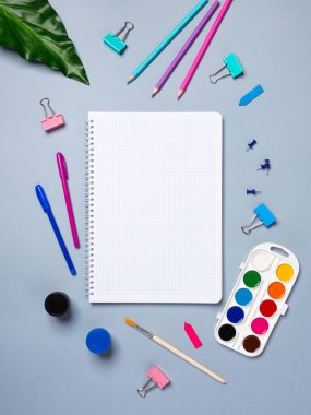 Kalem, kalem, suluboya ve diğer kırtasiyelerle dolu boş bir defter sayfası olan düz bir ofis masası. Üst manzara, düz uzanma.