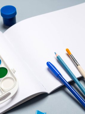 Açık arkaplan üzerinde suluboya, gouache, fırça ve diğer kırtasiye malzemelerinin olduğu boş çizim defterini aç, boşluğu kopyala