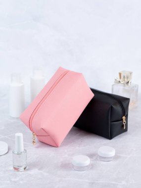 Taş bir masanın üzerinde renkli kozmetik poşetler, arka planda çiçekler ve parfüm.