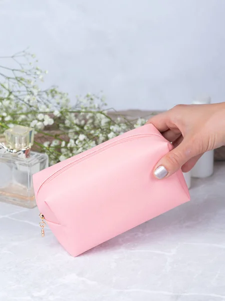 Leather pink cosmetic bag  on a stone table, with flowers and perfume in the background