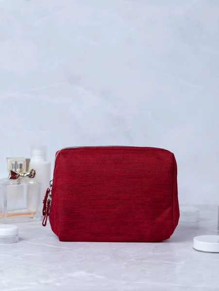 Red cosmetic bag  on a stone table, with flowers and perfume in the background