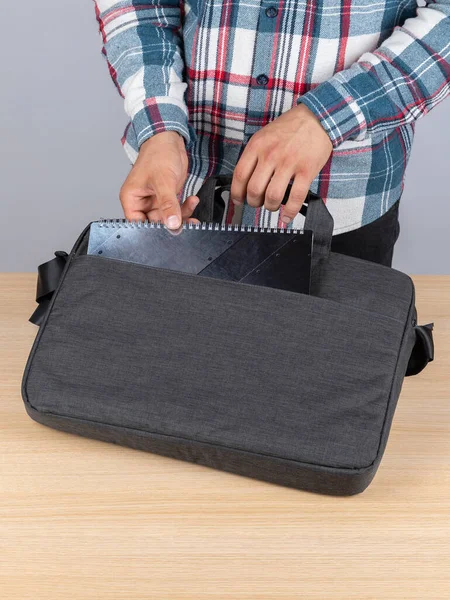 一个穿着格子呢衬衫的男人从一个时髦的背包里拿出一本黑色笔记本去工作 — 图库照片