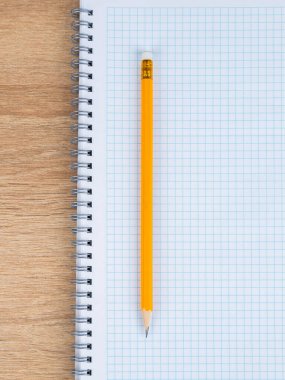 Damalı bir defterin üzerinde duran sarı bir tahta kalemin yakın plan görüntüsü, çalışmaya hazır.