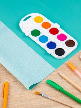 Resim masasının üzerindeki plastik koruyucu pedin, suluboya ve diğer kırtasiyelerin yanına yakın plan.