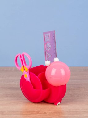 Pembe masaüstü organizatörü, mavi arka planda okul kırtasiyesi ve ofis malzemeleri var. Okula, ev ofisine, öğrenim konseptine geri dönmek.