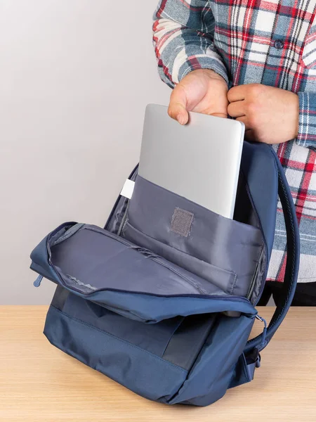 一个穿着格子呢衬衫的男人把他的手放在一个灰色的笔记本电脑上 上面有一个时髦的蓝色背包 — 图库照片