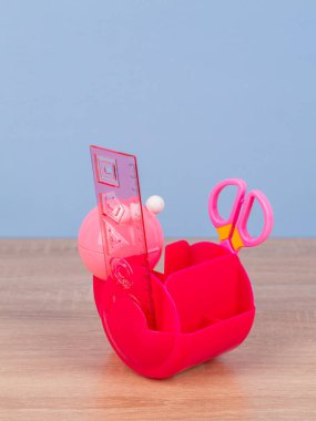 Pembe masaüstü organizatörü, mavi arka planda okul kırtasiyesi ve ofis malzemeleri var. Okula, ev ofisine, öğrenim konseptine geri dönmek.