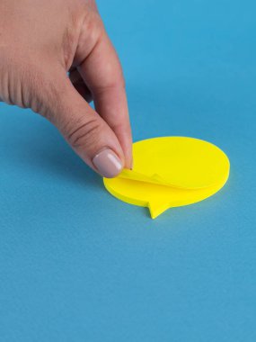 Yakın plan kadın, mavi arka planda izole edilmiş sarı boş kağıt yaprakları alıyor.