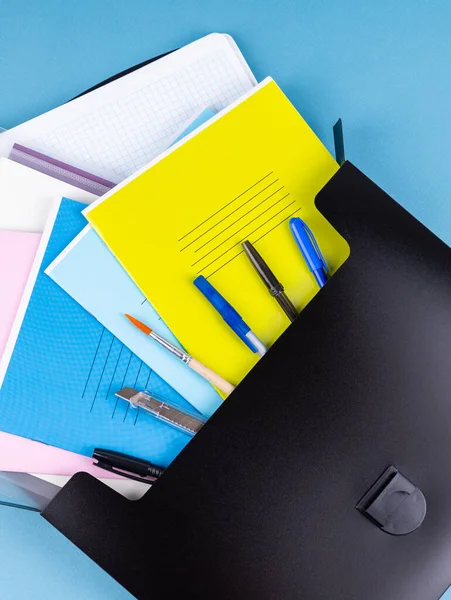 蓝色桌子上文具旁边的黑色塑料文件夹 用于文件和学习用品 — 图库照片