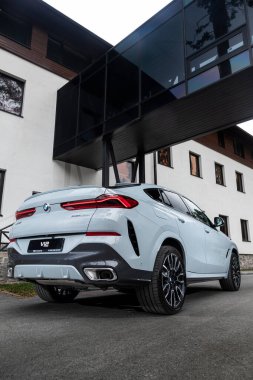 Novosibirsk, Rusya - 11 Ekim 2023: Sıcak bir yaz gününde beyaz BMW X6, binanın zeminine park etti. 