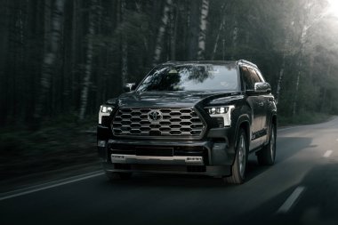 Novosibirsk, Rusya - Ekim 06, 2023: Gri Toyota Sequoia, sıcak bir günde bir ormanın arka planına karşı sokakta araba sürüyor.