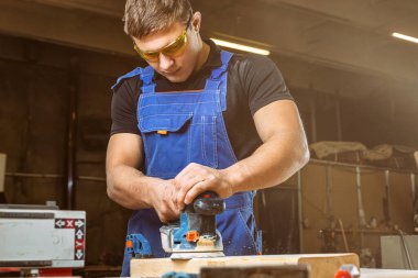 Parlatma makine veya rasgele yörünge sander atölye ile bir genç adam Oluşturucusu marangoz eşittir cilalar ahşap Yönetim Kurulu kapat