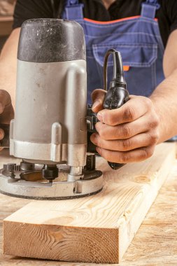 Erkek marangoz atölyedeki ahşap kalası cilalamak için elektrikli zımpara makinesi kullanıyor.