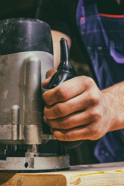 İş kıyafetleri içinde güçlü bir erkek marangoz hevesle çalışıyor ve bir sanayi atölyesinde ahşap bir masa üzerinde ahşap bir tahtayı kesiyor.