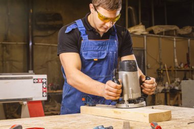  Genç bir esmer erkek marangoz, atölyede değirmen makinesi olan ahşap bir tahta parçasına eşittir.